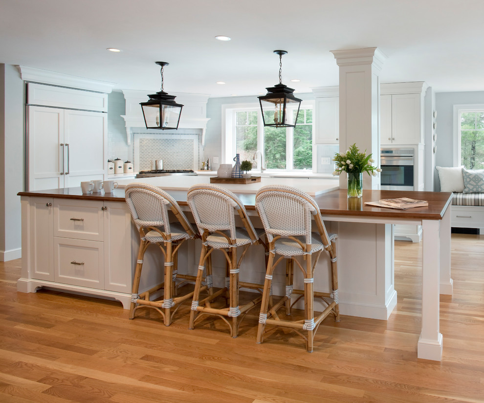 This is an example of a country l-shaped kitchen in Boston with shaker cabinets, white cabinets, panelled appliances, medium hardwood floors, with island, brown floor and white benchtop.