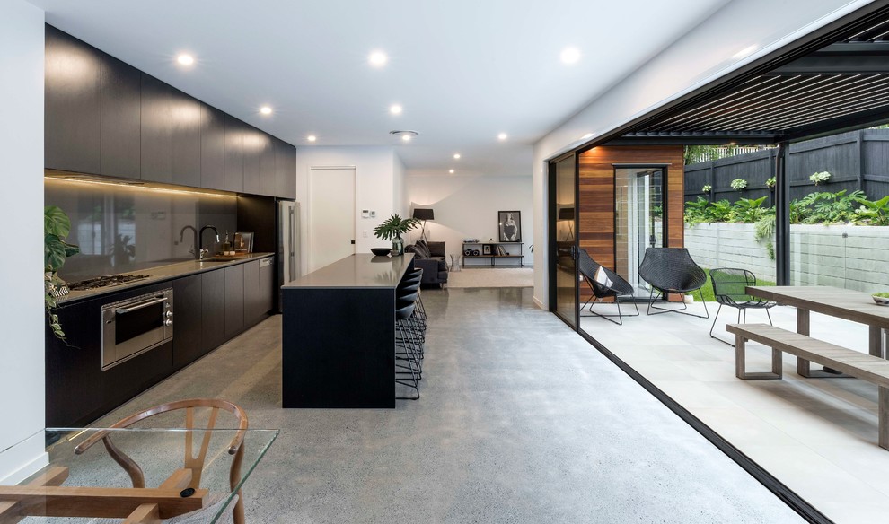 Inspiration for a contemporary galley open plan kitchen in Brisbane with an undermount sink, concrete floors, with island, flat-panel cabinets, dark wood cabinets, grey splashback, glass sheet splashback, stainless steel appliances, grey floor and grey benchtop.