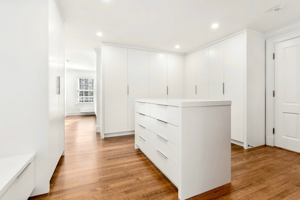 This is an example of a large contemporary gender-neutral walk-in wardrobe in Boston with white cabinets and medium hardwood floors.