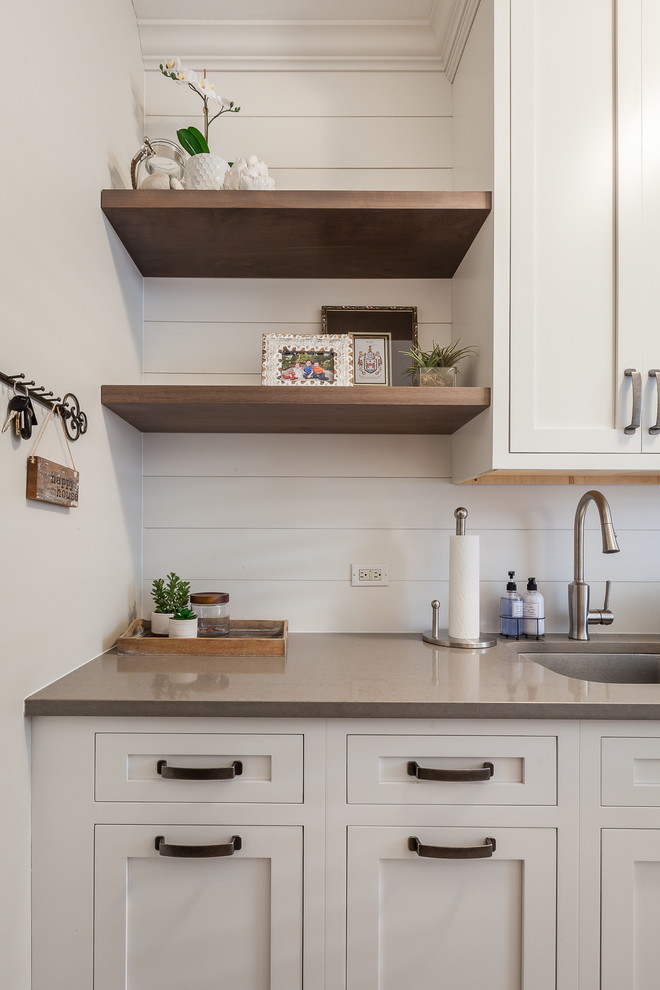 Inspiration for a mid-sized country single-wall utility room in Chicago with an undermount sink, recessed-panel cabinets, white cabinets, quartz benchtops, ceramic floors, a side-by-side washer and dryer, brown floor and white walls.