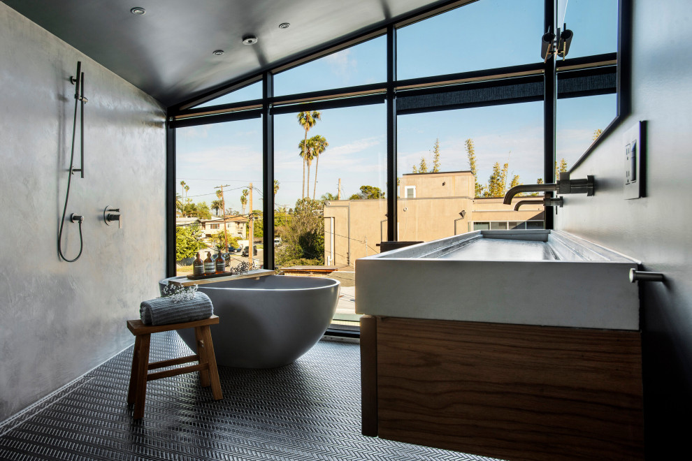 Inspiration for a medium sized urban ensuite bathroom in Los Angeles with a freestanding bath, a shower/bath combination, grey walls, a wall-mounted sink, an open shower, grey worktops, a wall niche, a single sink, a floating vanity unit, concrete worktops, black floors, medium wood cabinets, grey tiles and porcelain flooring.