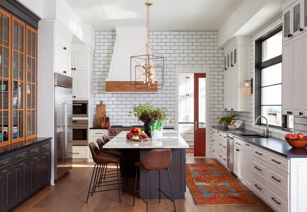 オースティンにある広いトランジショナルスタイルのおしゃれなキッチン (白いキャビネット、白いキッチンパネル、サブウェイタイルのキッチンパネル、シルバーの調理設備、茶色い床、黒いキッチンカウンター) の写真