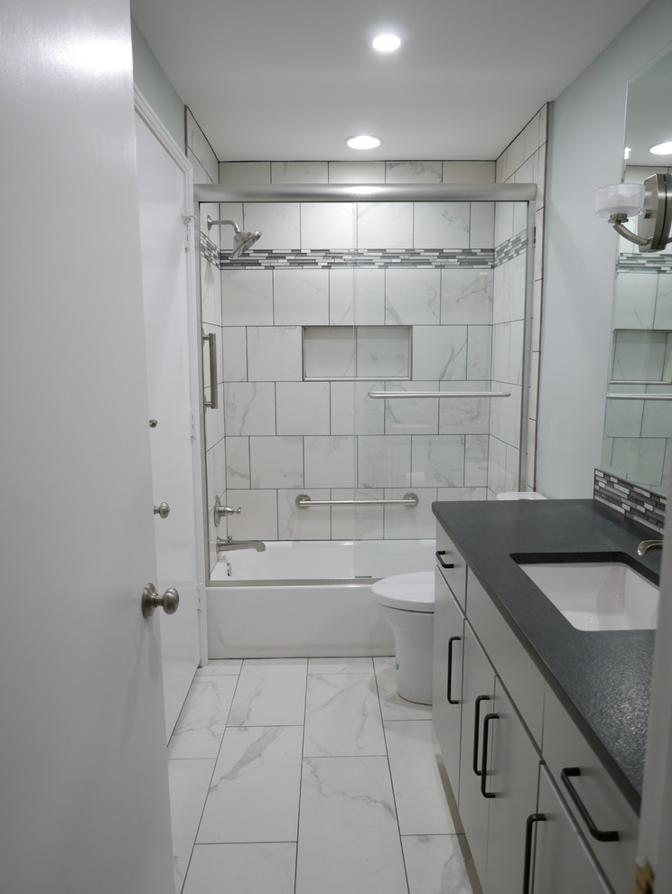This is an example of a mid-sized contemporary kids bathroom in Other with flat-panel cabinets, grey cabinets, an alcove tub, a shower/bathtub combo, a two-piece toilet, white tile, porcelain tile, green walls, porcelain floors, an undermount sink, granite benchtops, white floor, a sliding shower screen and black benchtops.