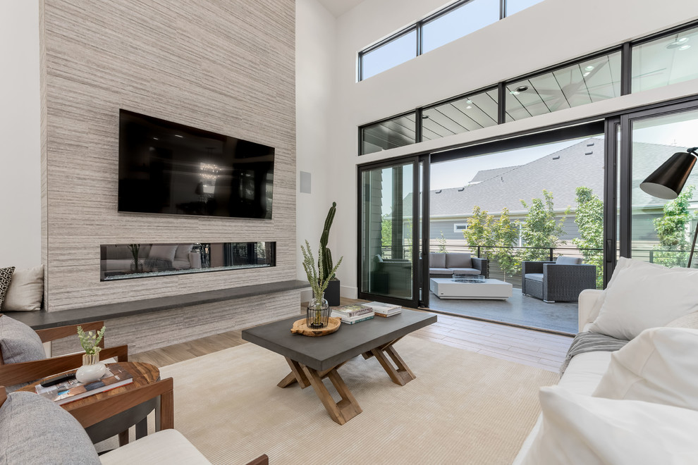 Large contemporary open concept family room in Salt Lake City with white walls, porcelain floors, a standard fireplace, a tile fireplace surround, a wall-mounted tv and beige floor.