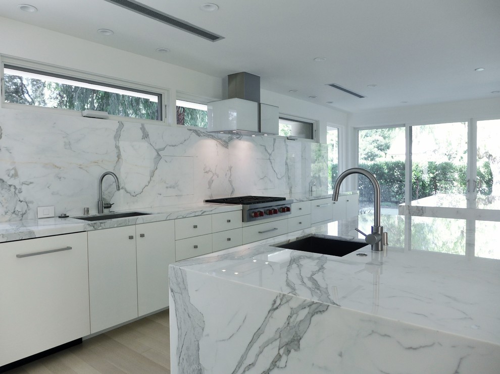 Photo of a large modern single-wall eat-in kitchen in Other with an undermount sink, flat-panel cabinets, white cabinets, marble benchtops, white splashback, stone slab splashback, stainless steel appliances, light hardwood floors and multiple islands.