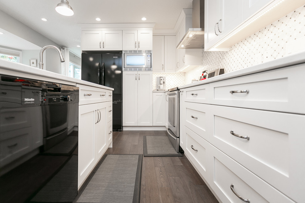 Eat-in kitchen - large transitional l-shaped medium tone wood floor and brown floor eat-in kitchen idea in Calgary with an undermount sink, shaker cabinets, white cabinets, quartz countertops, white backsplash, an island and black appliances
