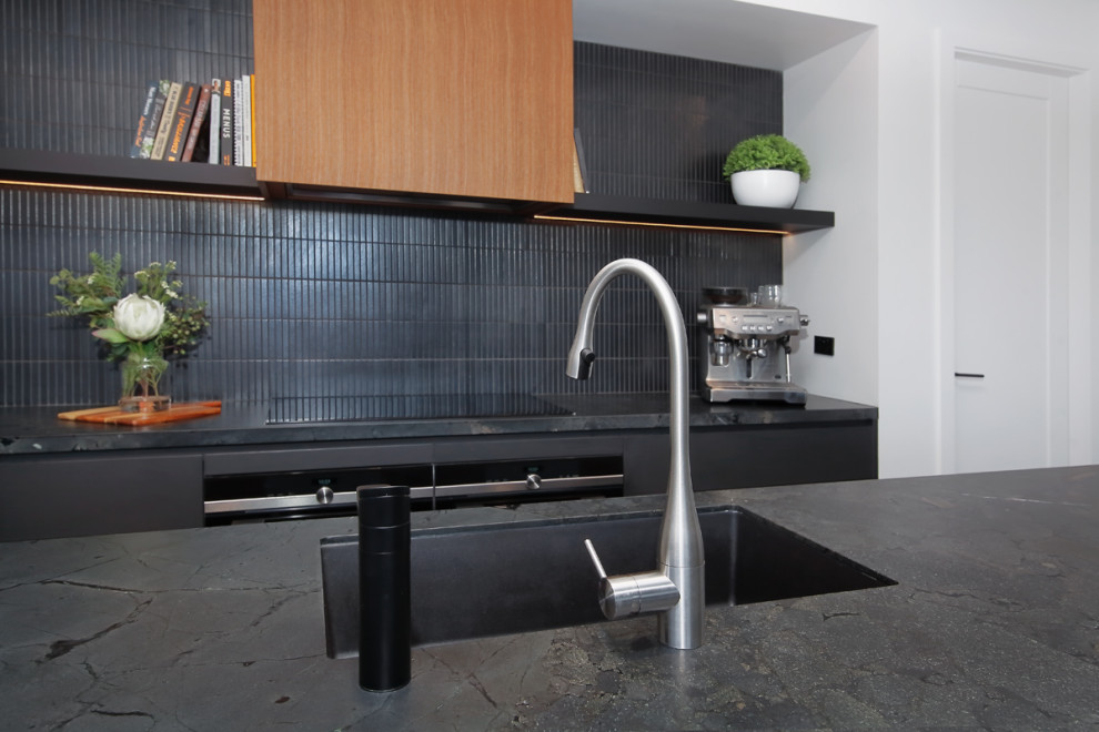 Mid-sized modern galley eat-in kitchen in Sydney with a double-bowl sink, flat-panel cabinets, brown cabinets, granite benchtops, black splashback, ceramic splashback, black appliances, cement tiles, with island, beige floor and black benchtop.