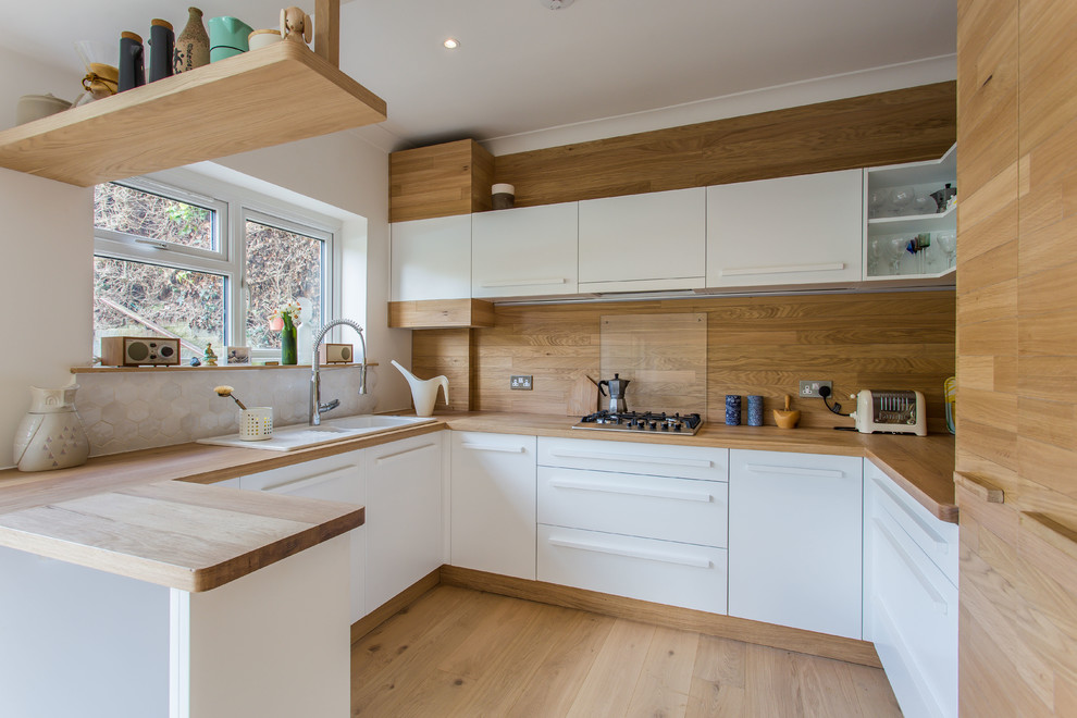 Scandinavian u-shaped kitchen in Sussex with a drop-in sink, flat-panel cabinets, white cabinets, wood benchtops, timber splashback, light hardwood floors and a peninsula.
