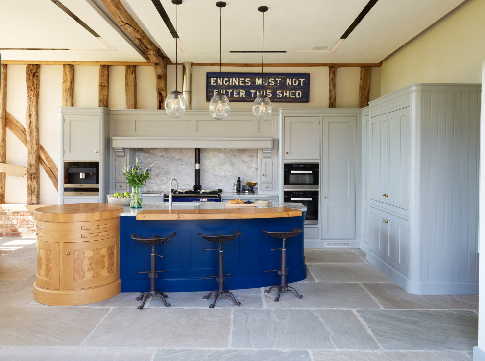 This is an example of a rural l-shaped kitchen/diner in Essex with a belfast sink, shaker cabinets, grey cabinets, granite worktops, grey splashback, granite splashback, black appliances, an island, grey floors and grey worktops.