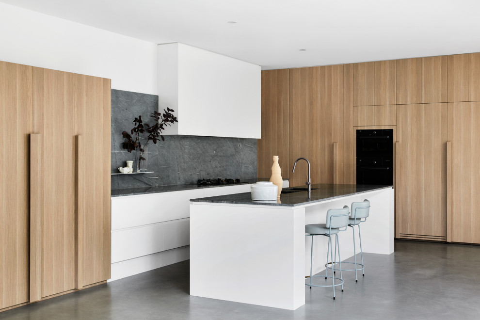 Photo of a mid-sized modern l-shaped kitchen pantry in Melbourne with an undermount sink, flat-panel cabinets, white cabinets, granite benchtops, blue splashback, stone slab splashback, black appliances, concrete floors, with island, grey floor and blue benchtop.