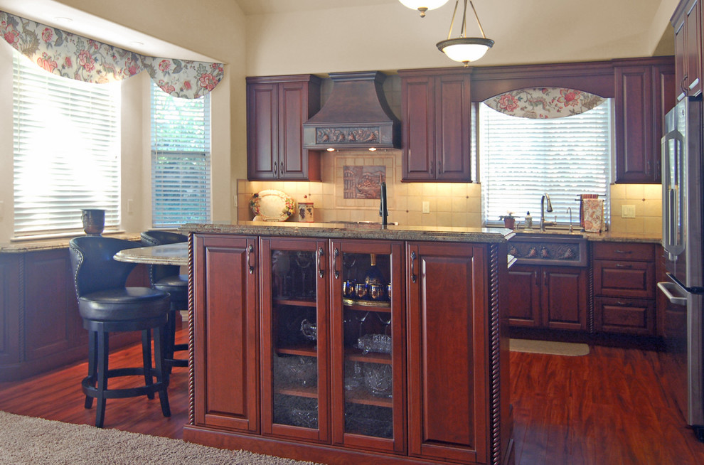 This is an example of a mid-sized traditional l-shaped open plan kitchen in San Luis Obispo with a farmhouse sink, raised-panel cabinets, red cabinets, granite benchtops, beige splashback, stone tile splashback, coloured appliances, dark hardwood floors and with island.