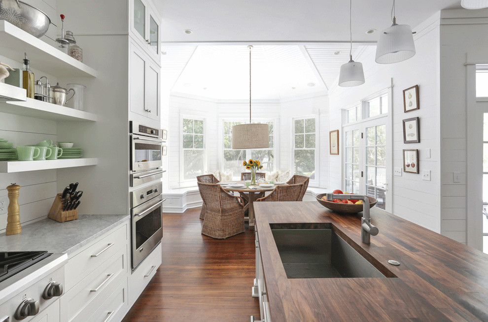 This is an example of a beach style eat-in kitchen in Charleston with a single-bowl sink, shaker cabinets, white cabinets, wood benchtops and stainless steel appliances.