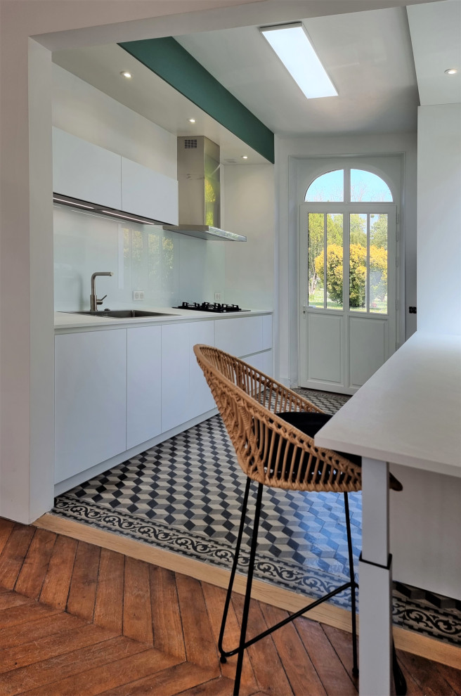 Inspiration for an expansive modern galley open plan kitchen in Other with an integrated sink, flat-panel cabinets, white cabinets, wood benchtops, white splashback, glass tile splashback, panelled appliances, cement tiles, no island, multi-coloured floor and white benchtop.