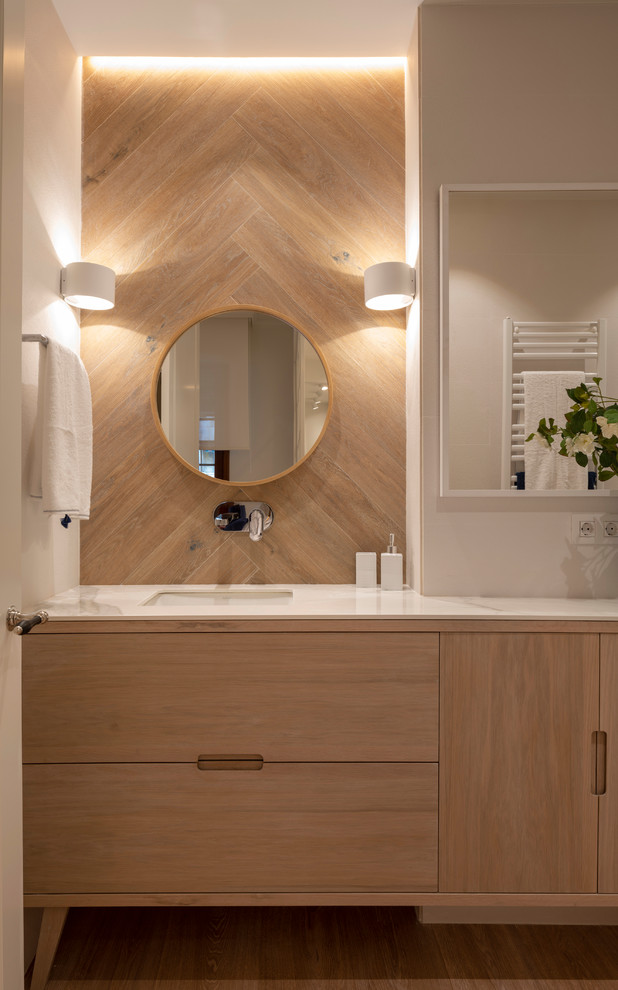 This is an example of a large contemporary bathroom in Bilbao with medium wood cabinets, white benchtops, beige tile, porcelain tile, beige walls, laminate floors, an undermount sink, marble benchtops, brown floor and flat-panel cabinets.