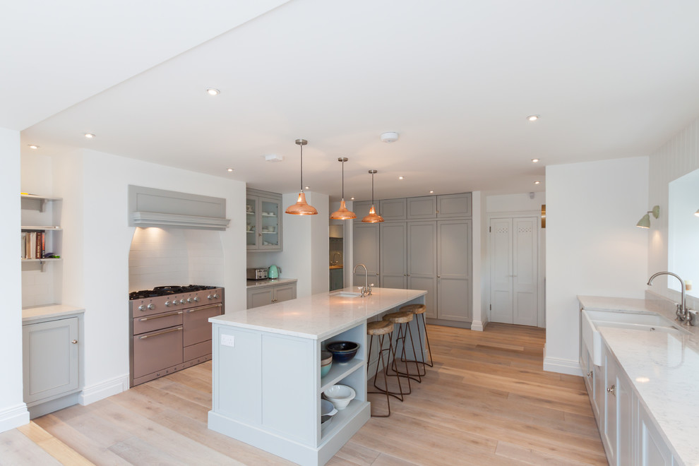This is an example of a large transitional galley kitchen in Other with recessed-panel cabinets, white cabinets, marble benchtops, white splashback, stainless steel appliances, light hardwood floors and with island.