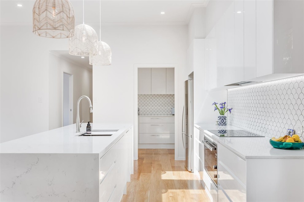 Contemporary galley kitchen pantry in Gold Coast - Tweed with an undermount sink, flat-panel cabinets, white cabinets, quartzite benchtops, white splashback, ceramic splashback, coloured appliances, medium hardwood floors, with island and brown floor.