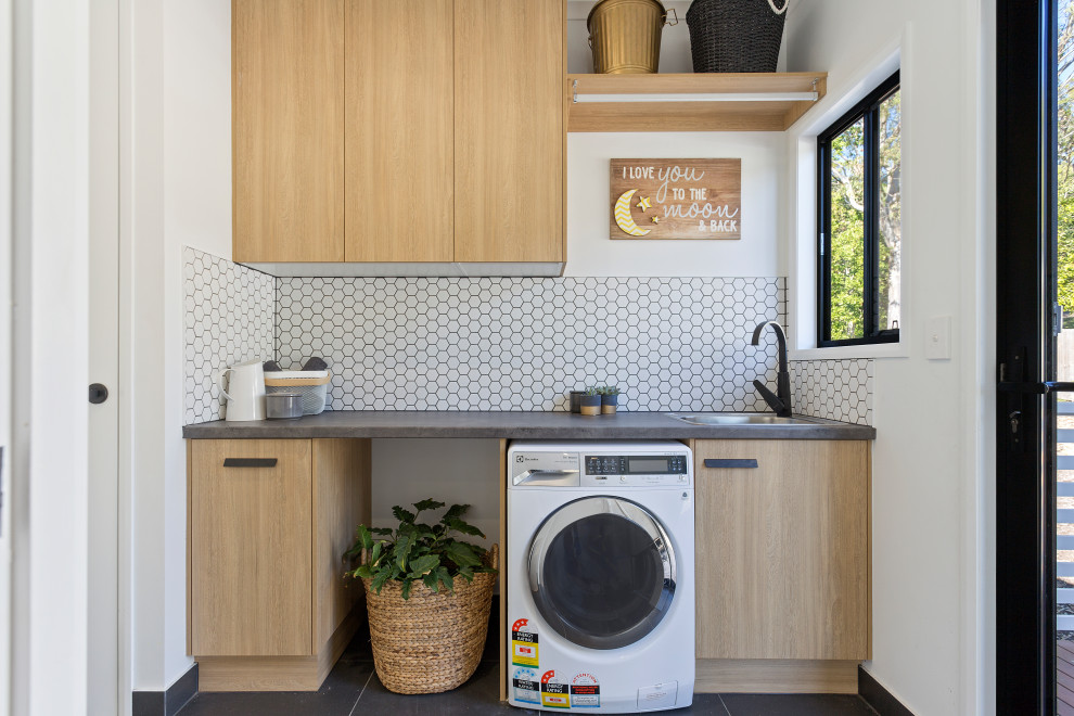This is an example of a small galley dedicated laundry room in Sunshine Coast with a drop-in sink, flat-panel cabinets, light wood cabinets, laminate benchtops, white splashback, ceramic splashback, white walls, ceramic floors and black floor.