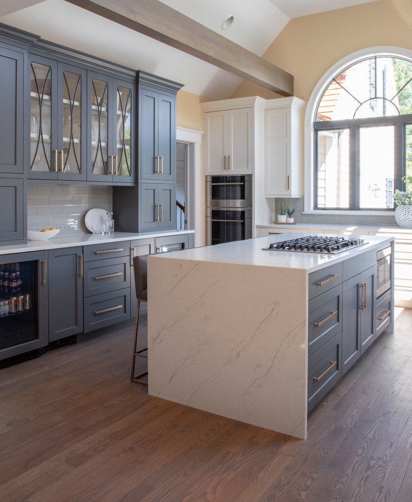 Example of a large transitional u-shaped medium tone wood floor kitchen design with an undermount sink, gray cabinets, quartz countertops, gray backsplash, glass tile backsplash, stainless steel appliances, an island and white countertops
