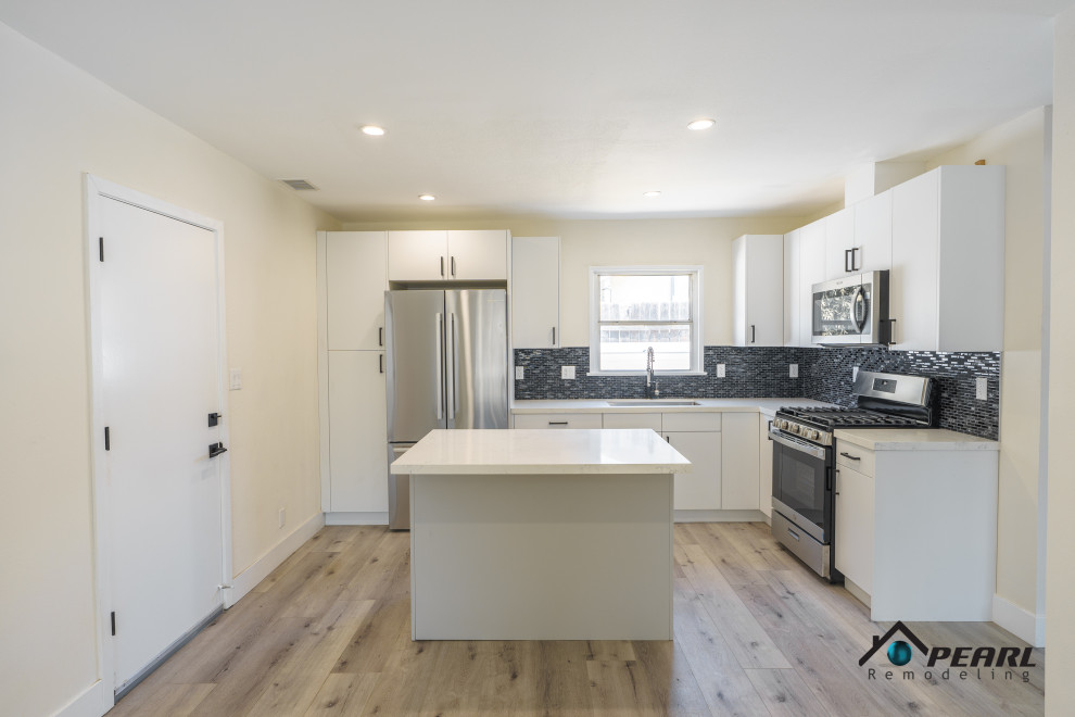 Photo of a small modern l-shaped eat-in kitchen in Los Angeles with a single-bowl sink, flat-panel cabinets, white cabinets, marble benchtops, black splashback, glass tile splashback, stainless steel appliances, light hardwood floors, with island, grey floor and white benchtop.