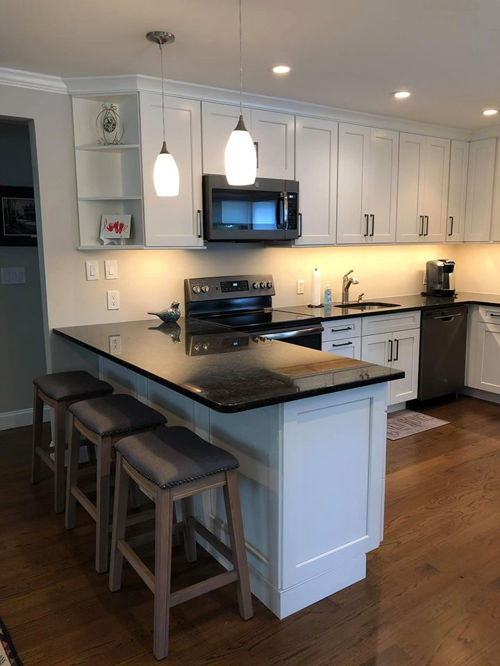 Photo of an u-shaped eat-in kitchen in New York with an undermount sink, shaker cabinets, white cabinets, granite benchtops, coloured appliances, medium hardwood floors, a peninsula, brown floor and black benchtop.