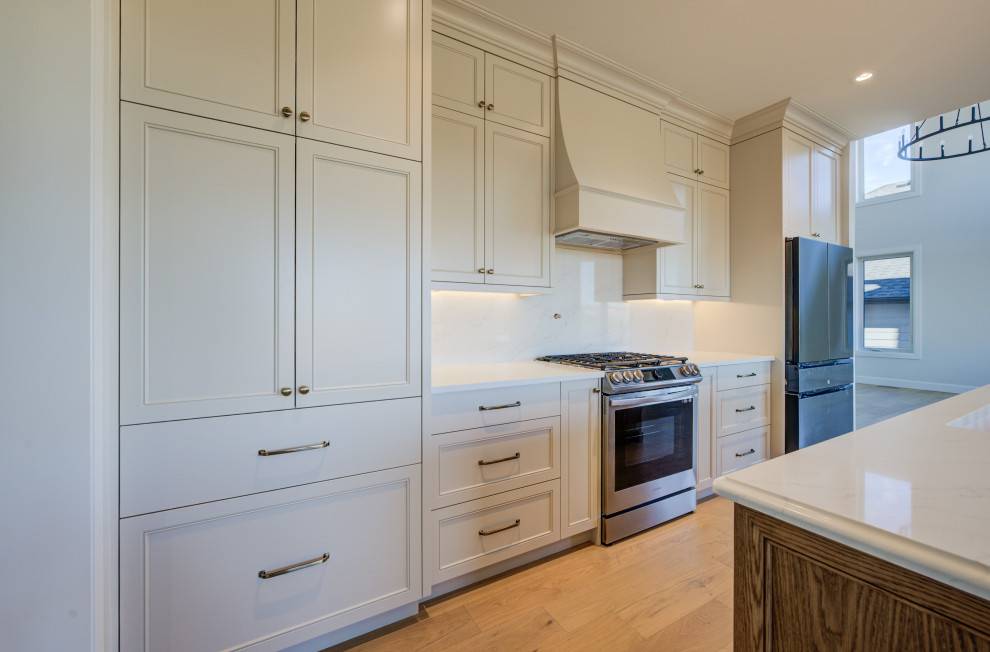 Mid-sized transitional single-wall light wood floor open concept kitchen photo in Toronto with an undermount sink, shaker cabinets, white cabinets, quartz countertops, white backsplash, quartz backsplash, stainless steel appliances, an island and white countertops