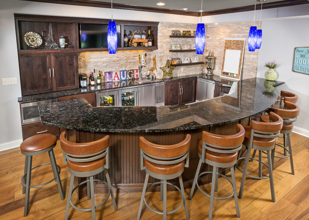 Inspiration for a large transitional u-shaped wet bar in Milwaukee with recessed-panel cabinets, dark wood cabinets, granite benchtops, beige splashback, stone tile splashback and medium hardwood floors.