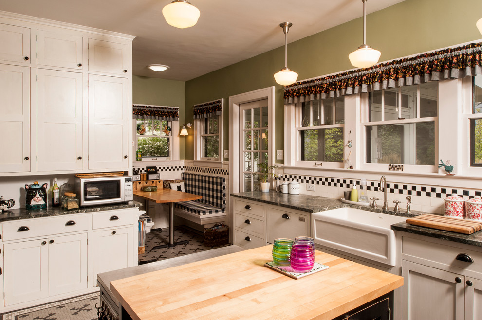 This is an example of a mid-sized traditional eat-in kitchen in Detroit with a farmhouse sink, shaker cabinets, white cabinets, granite benchtops, black splashback, subway tile splashback, black appliances, ceramic floors, with island and green benchtop.