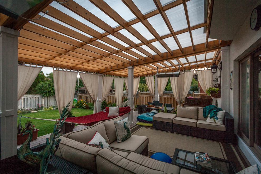 This is an example of a large transitional backyard deck in Toronto with a pergola.