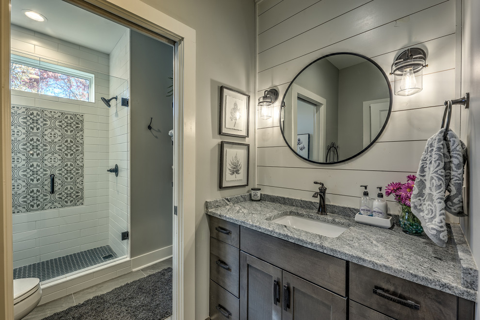 Mid-sized cottage 3/4 single-sink, ceramic tile, gray floor and shiplap wall bathroom photo in Atlanta with shaker cabinets, gray cabinets, a two-piece toilet, gray walls, an undermount sink, white countertops, a built-in vanity, granite countertops and a hinged shower door
