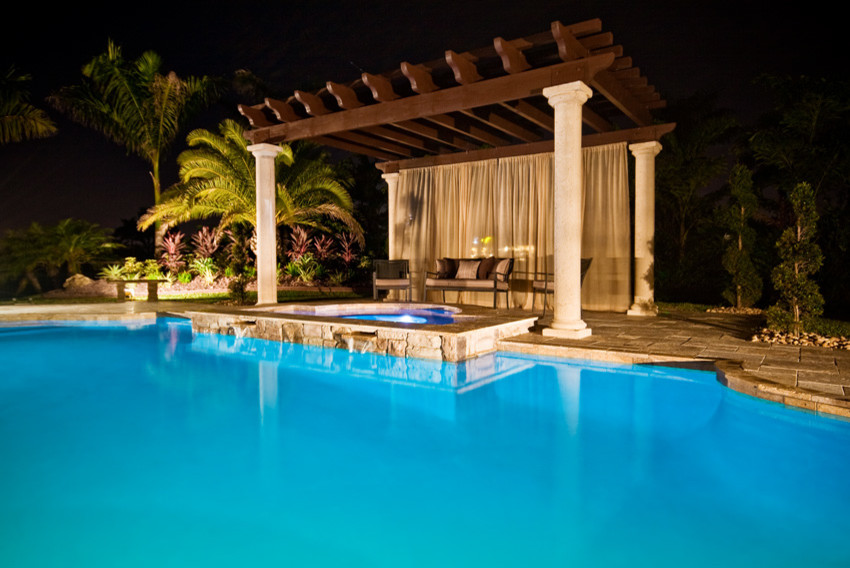 Large tropical backyard custom-shaped pool in Miami with a hot tub and natural stone pavers.