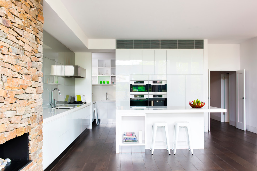 Design ideas for a mid-sized modern l-shaped kitchen in Melbourne with a double-bowl sink, flat-panel cabinets, white cabinets, quartz benchtops, grey splashback, glass sheet splashback, stainless steel appliances, dark hardwood floors and with island.
