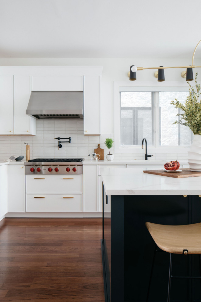 This is an example of a modern kitchen in Chicago with white splashback, subway tile splashback, stainless steel appliances, dark hardwood floors and with island.