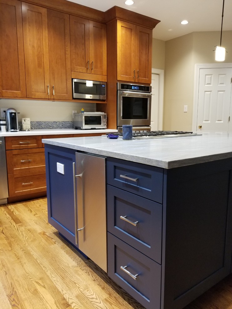 This is an example of a mid-sized transitional l-shaped eat-in kitchen in DC Metro with an integrated sink, recessed-panel cabinets, medium wood cabinets, solid surface benchtops, blue splashback, mosaic tile splashback, stainless steel appliances, medium hardwood floors, a peninsula, brown floor and blue benchtop.