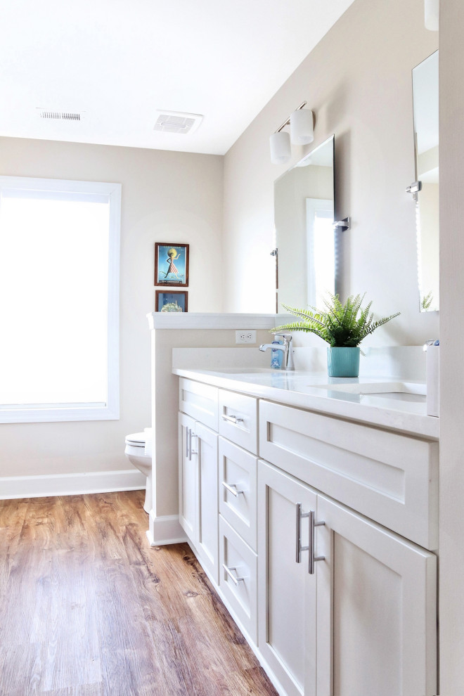 Mid-sized country kids bathroom in Other with shaker cabinets, white cabinets, a shower/bathtub combo, a two-piece toilet, beige walls, medium hardwood floors, an undermount sink, engineered quartz benchtops, brown floor, a shower curtain and white benchtops.