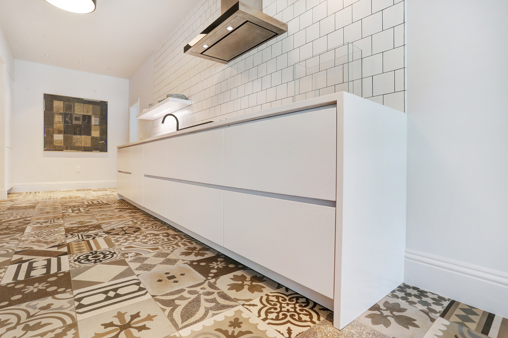 This is an example of a small eclectic galley separate kitchen in Miami with an undermount sink, flat-panel cabinets, white cabinets, solid surface benchtops, white splashback, porcelain splashback, stainless steel appliances, porcelain floors and no island.