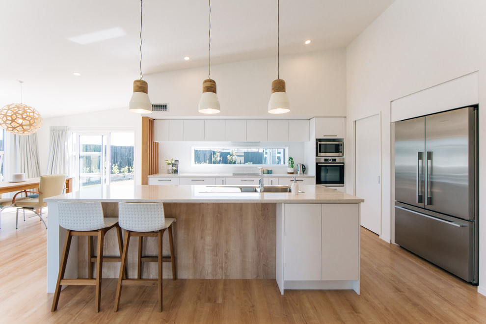 Scandinavian galley open plan kitchen in Christchurch with a drop-in sink, flat-panel cabinets, white cabinets, white splashback, stainless steel appliances, medium hardwood floors, with island, beige floor and beige benchtop.