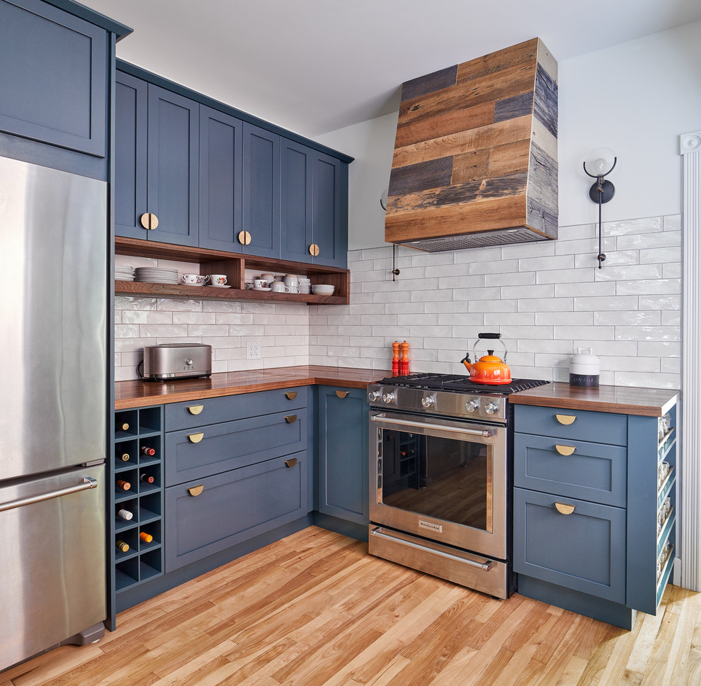 Small transitional l-shaped kitchen in Ottawa with blue cabinets, wood benchtops, white splashback, stainless steel appliances, brown benchtop, shaker cabinets, subway tile splashback and light hardwood floors.