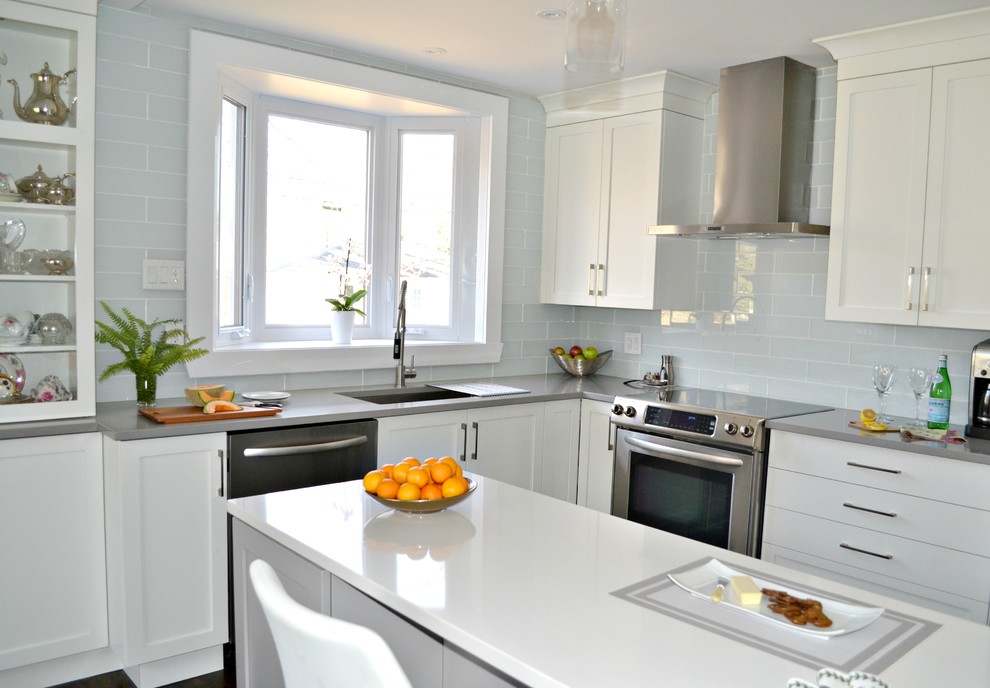 This is an example of a mid-sized contemporary l-shaped eat-in kitchen in Montreal with an undermount sink, shaker cabinets, white cabinets, quartz benchtops, white splashback, glass tile splashback, stainless steel appliances, medium hardwood floors and with island.