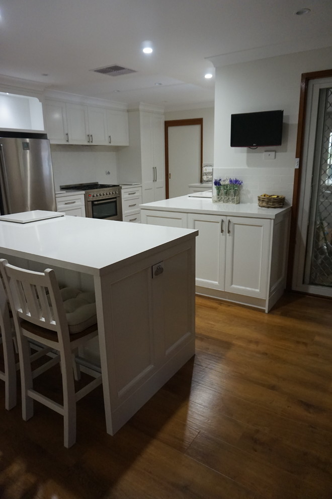 This is an example of a large contemporary eat-in kitchen in Sydney with a drop-in sink, recessed-panel cabinets, white cabinets, quartz benchtops, white splashback, porcelain splashback, stainless steel appliances, light hardwood floors and with island.