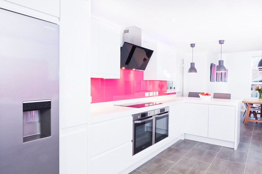 Design ideas for a mid-sized contemporary galley eat-in kitchen in Buckinghamshire with flat-panel cabinets, white cabinets, solid surface benchtops, pink splashback, glass sheet splashback, stainless steel appliances, vinyl floors, a peninsula and an integrated sink.