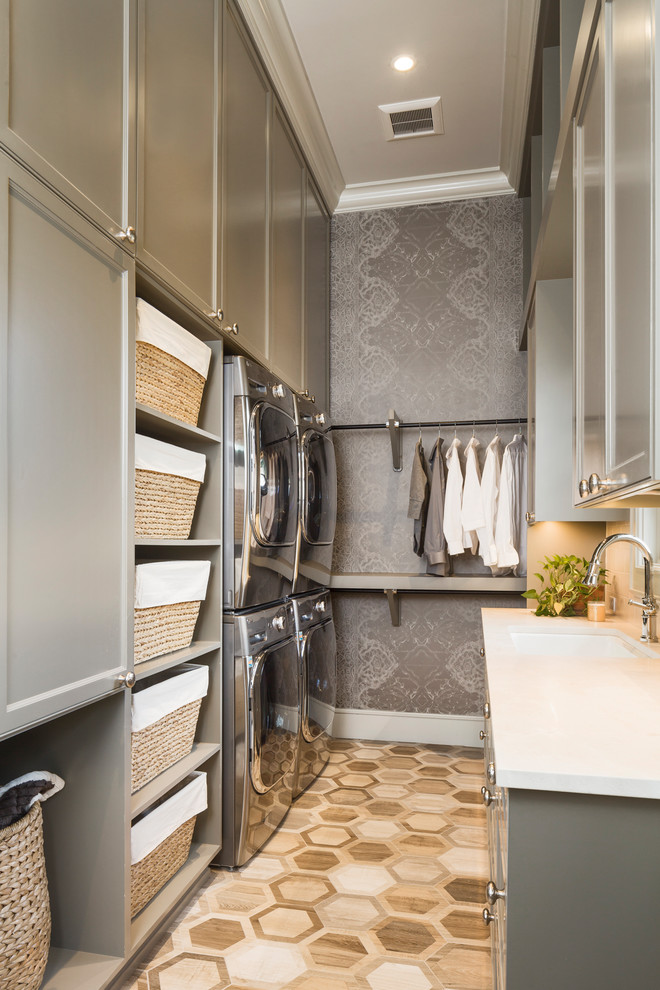 Design ideas for a mid-sized transitional galley dedicated laundry room in Austin with an undermount sink, recessed-panel cabinets, grey cabinets, marble benchtops, grey walls, porcelain floors, a stacked washer and dryer, brown floor and white benchtop.