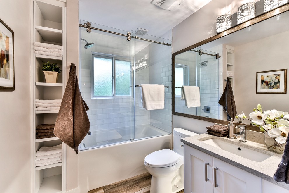 Photo of a mid-sized transitional bathroom in Vancouver with shaker cabinets, white cabinets, a one-piece toilet, gray tile, ceramic tile, grey walls, ceramic floors, an undermount sink, quartzite benchtops, an alcove tub, a shower/bathtub combo and a sliding shower screen.