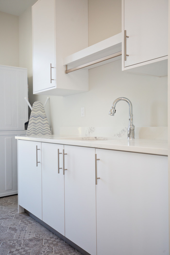 Foto på en mellanstor funkis vita linjär tvättstuga enbart för tvätt, med en nedsänkt diskho, släta luckor, vita skåp, bänkskiva i kvarts, vitt stänkskydd, vita väggar, klinkergolv i keramik, en tvättpelare och grått golv