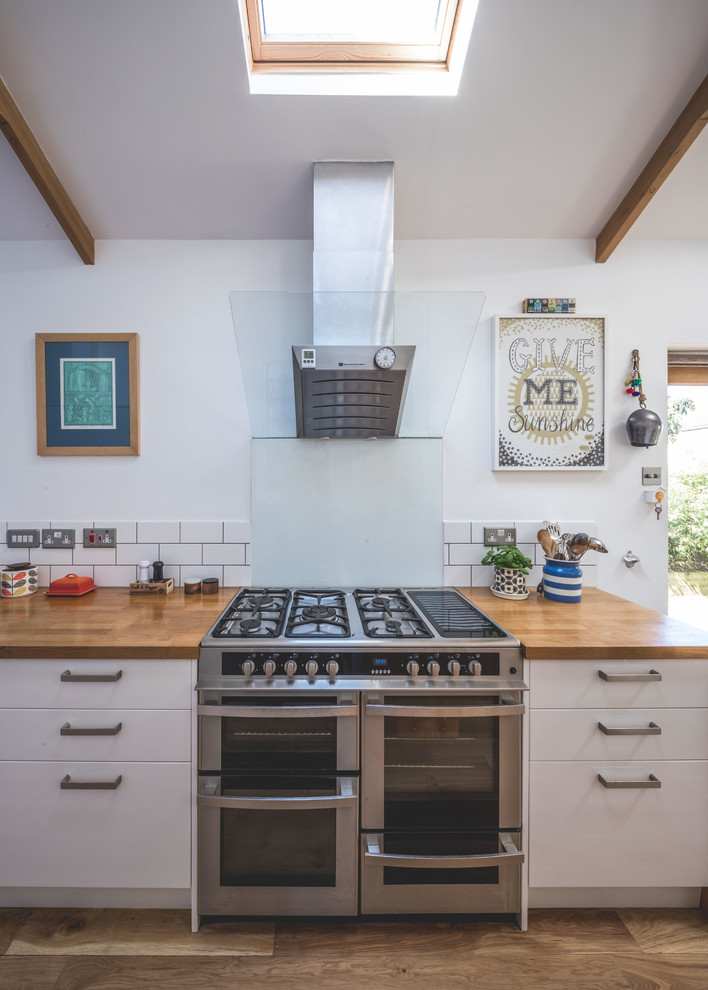 Design ideas for a mid-sized contemporary galley open plan kitchen in Other with an undermount sink, flat-panel cabinets, white cabinets, wood benchtops, white splashback, subway tile splashback, panelled appliances, medium hardwood floors, a peninsula, brown floor and brown benchtop.