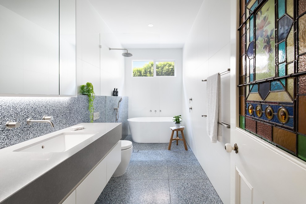 This is an example of a contemporary bathroom in Melbourne with flat-panel cabinets, white cabinets, a freestanding tub, a curbless shower, black and white tile, white tile, white walls, an undermount sink, black floor, an open shower and grey benchtops.