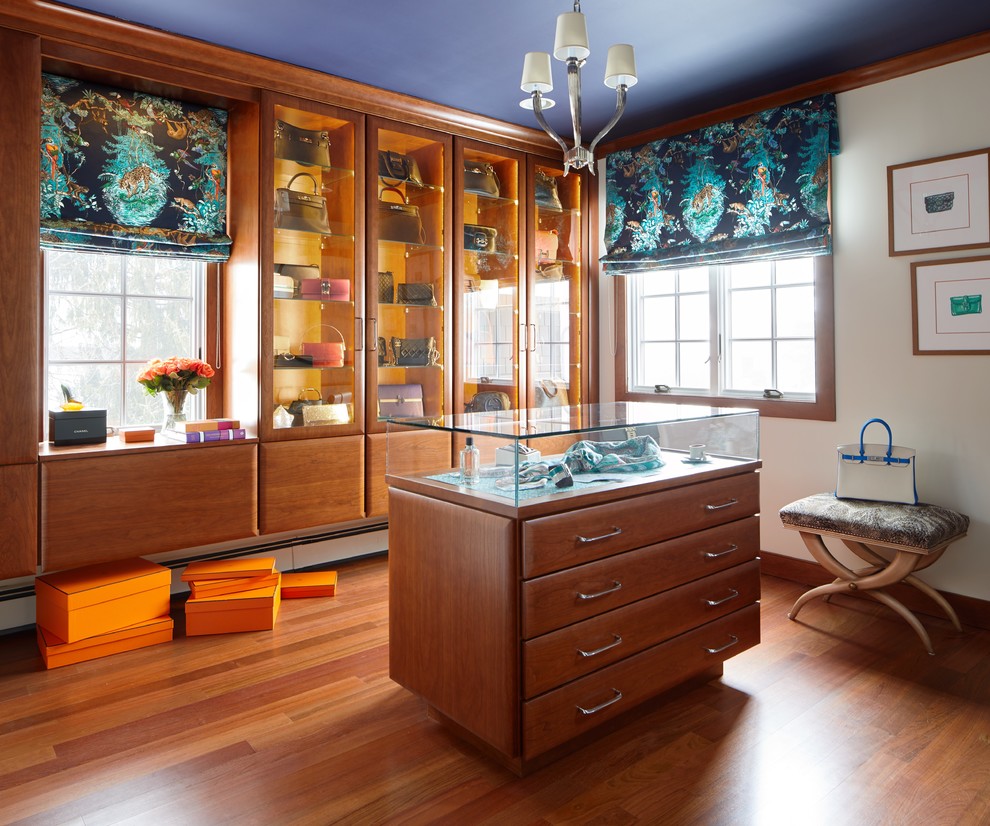 This is an example of a mid-sized transitional women's walk-in wardrobe in New York with glass-front cabinets, medium wood cabinets, medium hardwood floors and orange floor.