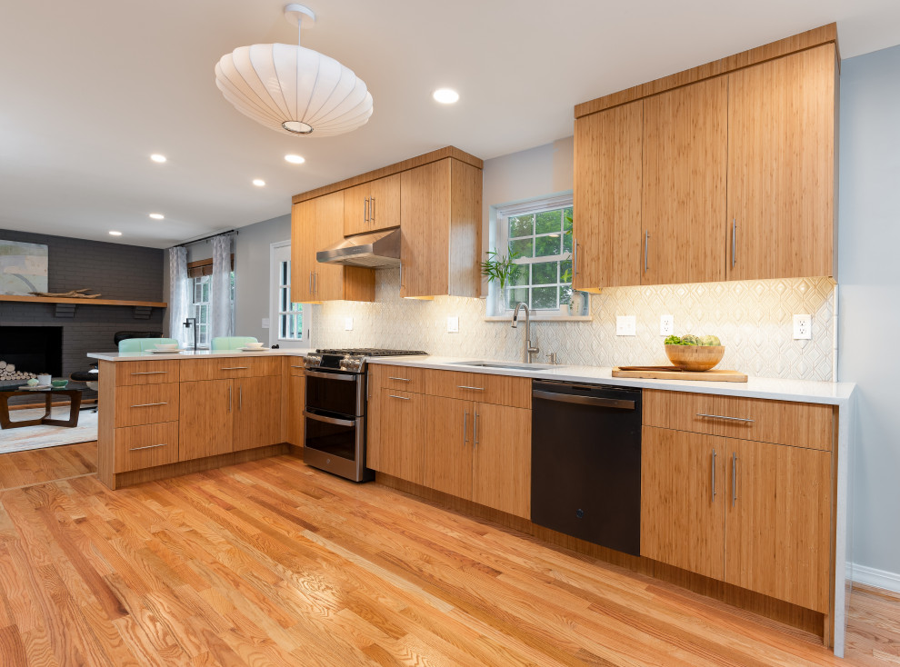 This is an example of a mid-sized midcentury galley eat-in kitchen in Cincinnati with an undermount sink, light wood cabinets, quartz benchtops, grey splashback, mosaic tile splashback, black appliances, light hardwood floors and white benchtop.