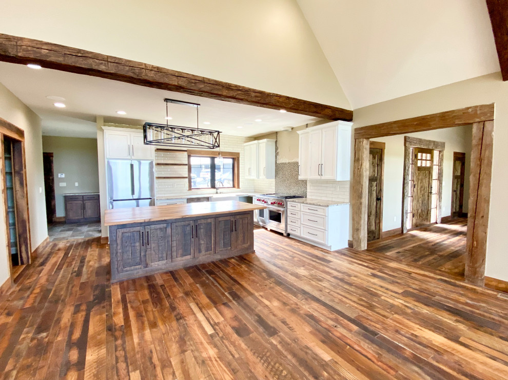 Photo of a mid-sized country l-shaped open plan kitchen in Kansas City with a farmhouse sink, shaker cabinets, dark wood cabinets, wood benchtops, white splashback, shiplap splashback, stainless steel appliances, medium hardwood floors, with island, brown floor and brown benchtop.