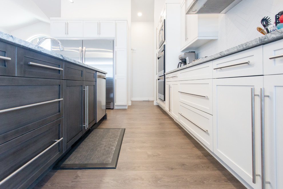 Mid-sized contemporary l-shaped open plan kitchen in Calgary with an undermount sink, shaker cabinets, white cabinets, granite benchtops, white splashback, ceramic splashback, stainless steel appliances, medium hardwood floors and with island.