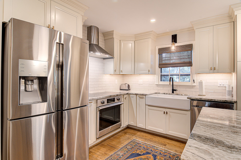 Inspiration for a mid-sized transitional l-shaped medium tone wood floor and brown floor eat-in kitchen remodel with a farmhouse sink, recessed-panel cabinets, white cabinets, marble countertops, white backsplash, subway tile backsplash, stainless steel appliances, an island and gray countertops